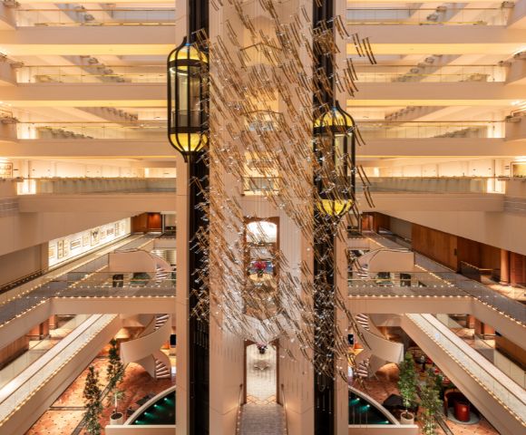 Spacious hotel atrium with multiple floors, modern decor, glass elevators, and warm lighting. Symmetrical design evokes elegance and grandeur.