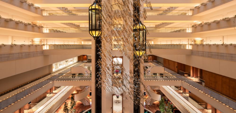 Spacious hotel atrium with multiple floors, modern decor, glass elevators, and warm lighting. Symmetrical design evokes elegance and grandeur.