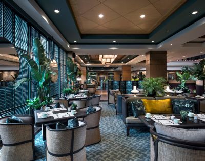 The elegant restaurant interior features wicker chairs, patterned carpets, and lush green plants, creating a cozy and inviting atmosphere.