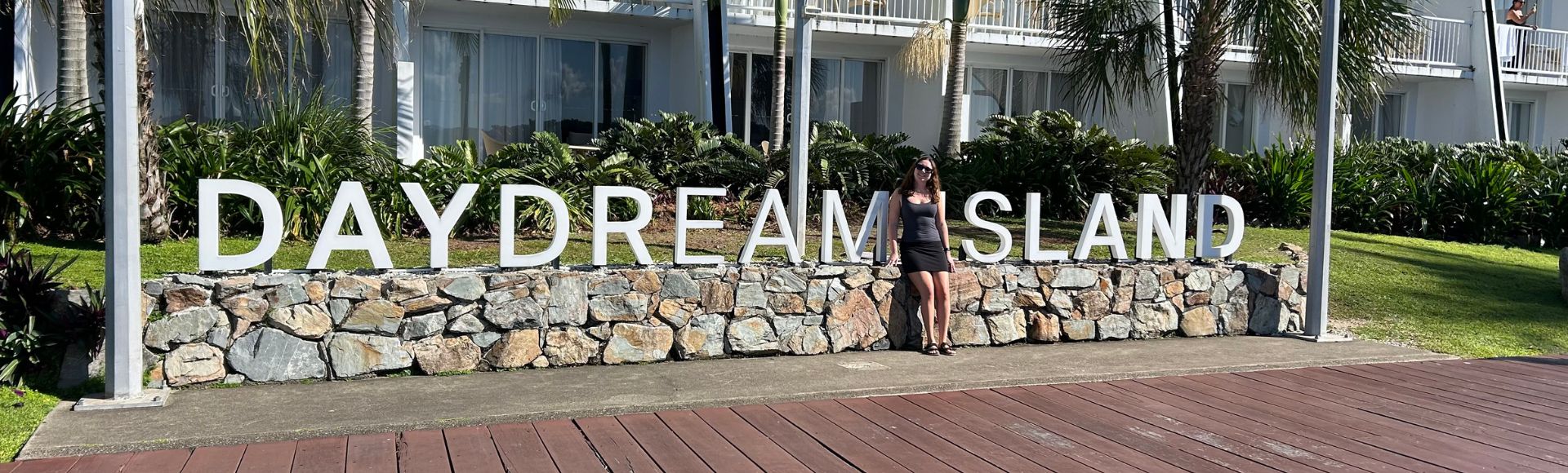 A person stands by a stone wall with large white letters spelling 