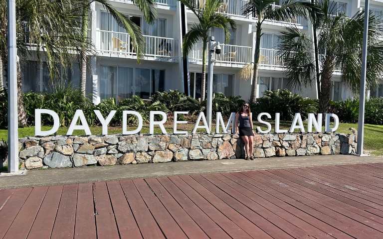 A person stands by a stone wall with large white letters spelling 