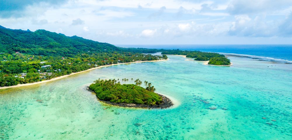 Aerial view of a tropical island with lush greenery, surrounded by turquoise water and smaller islets, under a partly cloudy sky. Peaceful and idyllic scene.