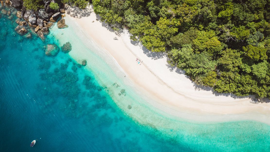 Aerial view of a secluded tropical beach bordered by lush green forest on one side and clear turquoise ocean on the other. Peaceful and serene setting.