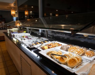 A buffet with various pastries and desserts displayed on white trays, under warm lighting, creating an inviting and cozy atmosphere.