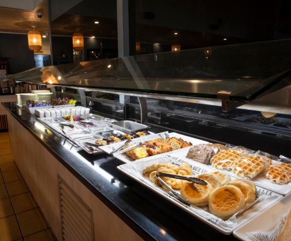 A buffet with various pastries and desserts displayed on white trays, under warm lighting, creating an inviting and cozy atmosphere.