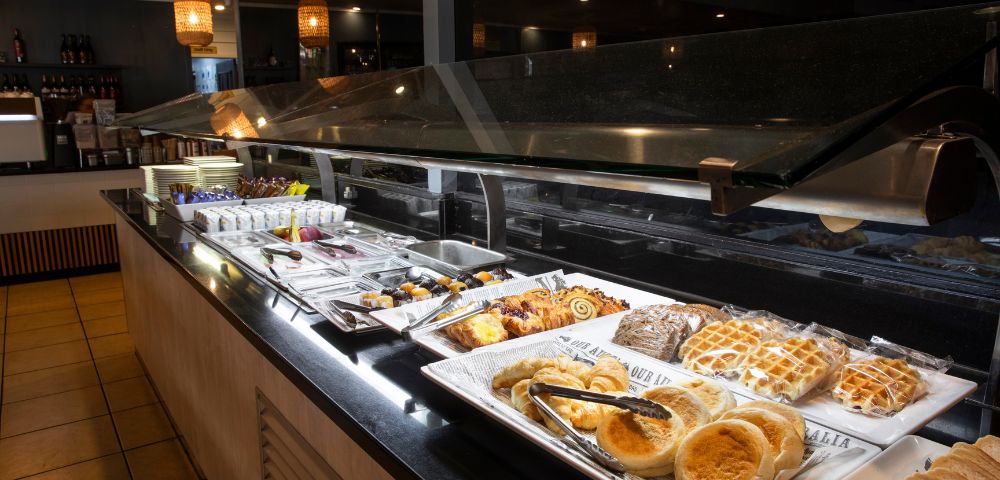 A buffet with various pastries and desserts displayed on white trays, under warm lighting, creating an inviting and cozy atmosphere.