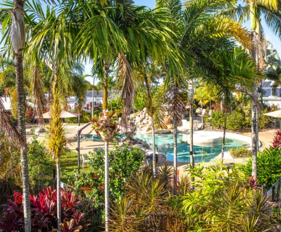Tropical oasis featuring lush palm trees and vibrant foliage surrounding a serene pool with a waterfall. The scene conveys relaxation and tranquility.