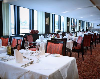 Luxurious restaurant with elegant decor, white tablecloths, red chairs, and soft lighting. Large windows provide natural light and a serene atmosphere.