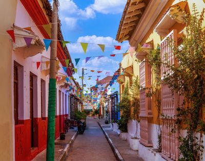 Colorful street with vibrant buildings and festive pennant flags strung above. Sunny day with a clear blue sky. Quaint and lively atmosphere.