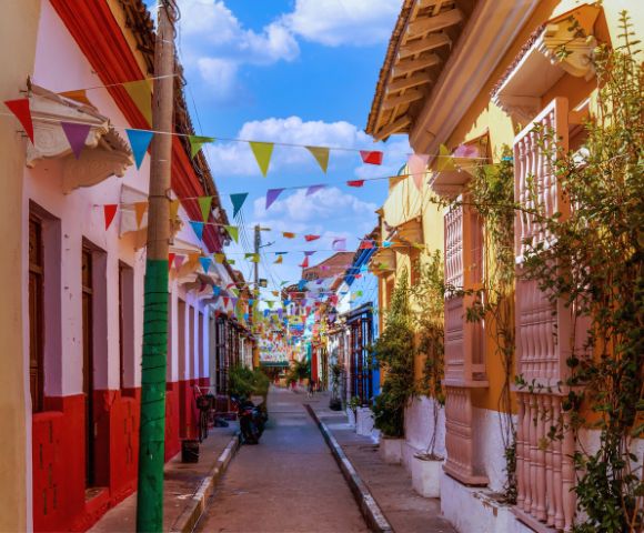 Colorful street with vibrant buildings and festive pennant flags strung above. Sunny day with a clear blue sky. Quaint and lively atmosphere.