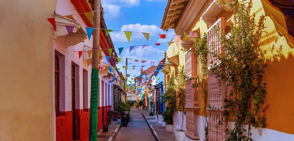 Colorful street with vibrant buildings and festive pennant flags strung above. Sunny day with a clear blue sky. Quaint and lively atmosphere.