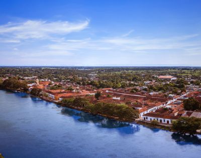 Aerial view of a historic town by a river, featuring red-tiled roofs and white colonial buildings. The scene conveys a serene and timeless atmosphere.