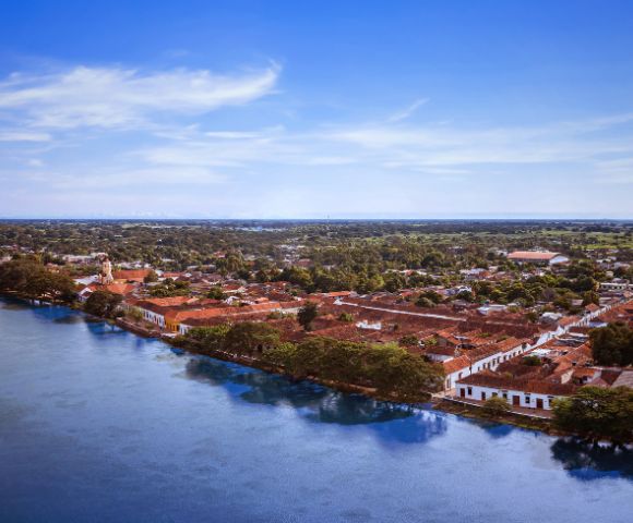 Aerial view of a historic town by a river, featuring red-tiled roofs and white colonial buildings. The scene conveys a serene and timeless atmosphere.