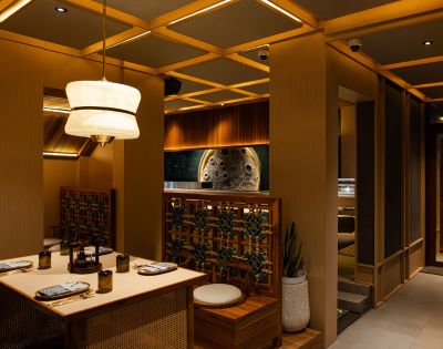 Cozy upscale restaurant interior featuring warm lighting, a wooden table set for dining, elegant pendant lights, and lush greenery accents.