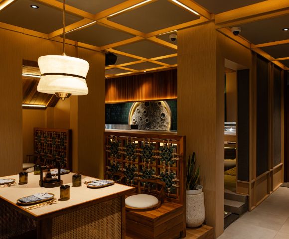Cozy upscale restaurant interior featuring warm lighting, a wooden table set for dining, elegant pendant lights, and lush greenery accents.