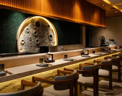 A modern, elegant sushi bar with wooden chairs, a textured circular wall art resembling the moon, warm lighting, and a minimalist design.