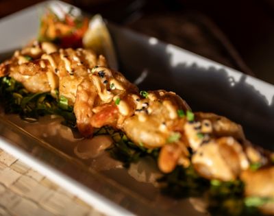 A close-up of a gourmet dish featuring grilled seafood topped with sauce and sesame seeds, on a bed of greens. Bright, appetizing presentation.