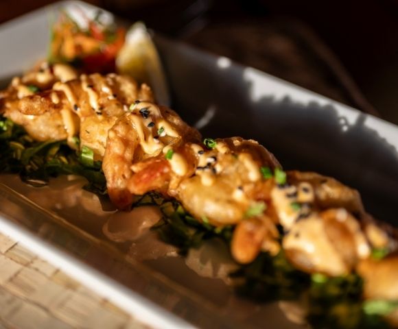 A close-up of a gourmet dish featuring grilled seafood topped with sauce and sesame seeds, on a bed of greens. Bright, appetizing presentation.