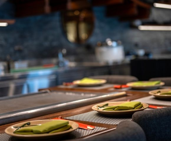 A sleek, modern kitchen setup with a row of elegant place settings, featuring green napkins and red chopsticks, creates a welcoming dining atmosphere.