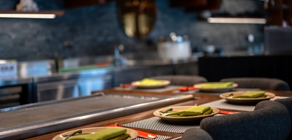 A sleek, modern kitchen setup with a row of elegant place settings, featuring green napkins and red chopsticks, creates a welcoming dining atmosphere.