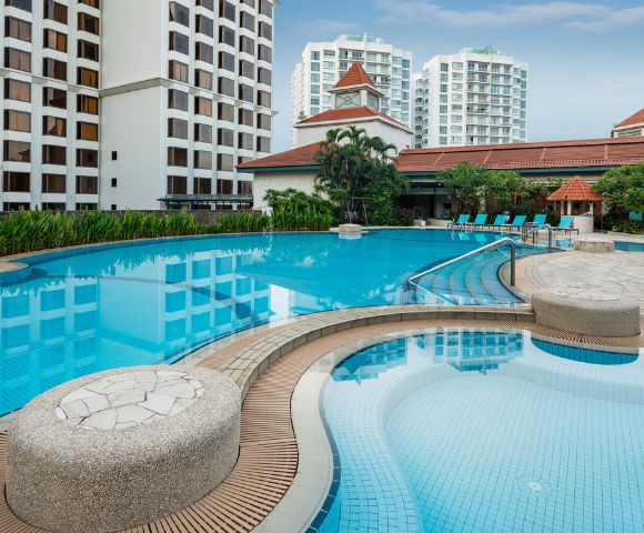 Luxurious outdoor pool scene with clear, blue water surrounded by elegant, tall buildings and lush greenery, evoking a tranquil and relaxing atmosphere.