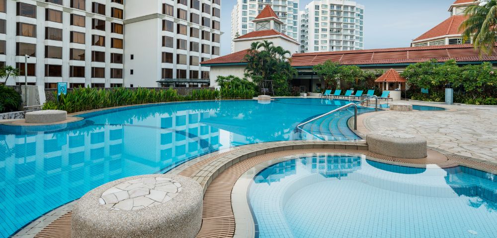 Luxurious outdoor pool scene with clear, blue water surrounded by elegant, tall buildings and lush greenery, evoking a tranquil and relaxing atmosphere.