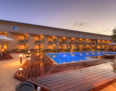 Elegant resort at sunset with a glowing blue pool, surrounded by palm trees and loungers. The tranquil ambiance suggests relaxation and luxury.