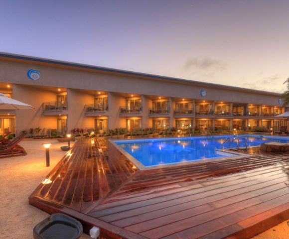 Elegant resort at sunset with a glowing blue pool, surrounded by palm trees and loungers. The tranquil ambiance suggests relaxation and luxury.