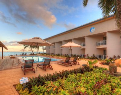 Resort poolside area with lounge chairs and umbrellas, surrounded by lush greenery and palm trees at sunset, evoking a peaceful, tropical ambiance.