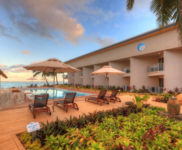 Resort poolside area with lounge chairs and umbrellas, surrounded by lush greenery and palm trees at sunset, evoking a peaceful, tropical ambiance.