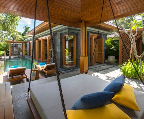 Luxurious tropical villa with a private pool, surrounded by lush greenery. Features a cozy outdoor swing bed with blue and yellow cushions, exuding relaxation.