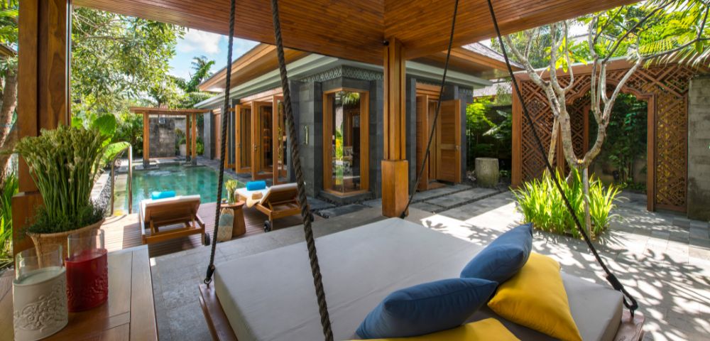Luxurious tropical villa with a private pool, surrounded by lush greenery. Features a cozy outdoor swing bed with blue and yellow cushions, exuding relaxation.
