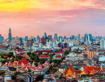 Skyline of a bustling city at sunset, with modern skyscrapers and traditional red-roofed temples. The vibrant sky adds warmth and a sense of tranquility.