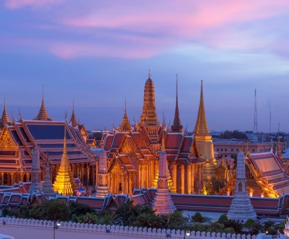 Golden temple spires and rooftops illuminated at dusk under a vibrant pink and blue sky, creating a serene and majestic atmosphere.