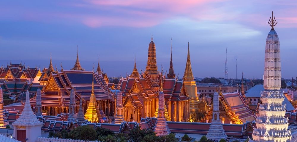 Golden temple spires and rooftops illuminated at dusk under a vibrant pink and blue sky, creating a serene and majestic atmosphere.