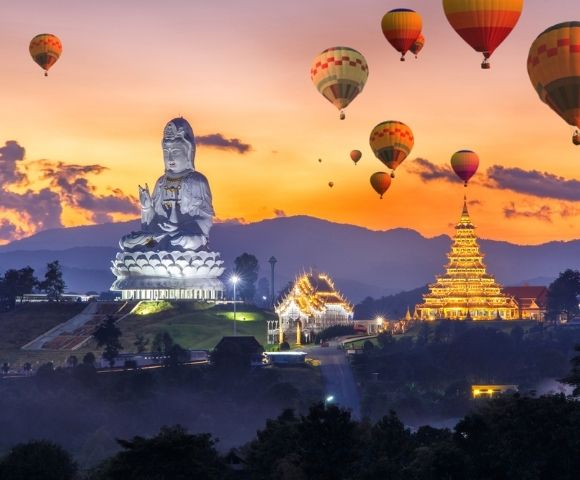 Sunset over Chiang Rai with a giant white Buddha statue and golden temple, surrounded by colorful hot air balloons in a serene, majestic landscape.