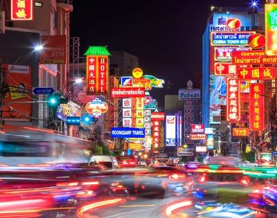 A vibrant city street illuminated by colorful neon signs in various languages, bustling with blurred car lights and activity, exuding a dynamic nightlife energy.