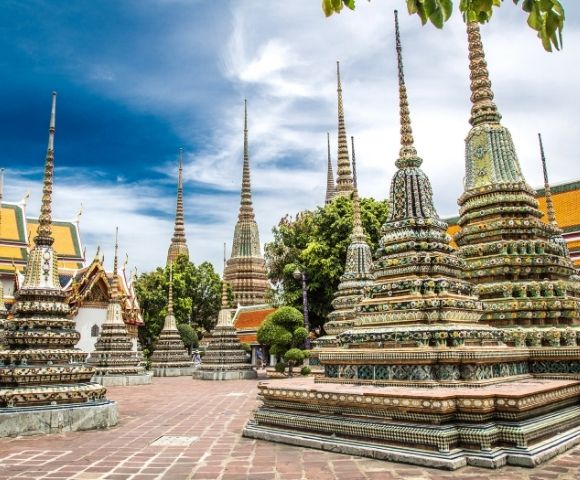 Colorful and ornate stupas of Wat Pho in Bangkok, Thailand, stand under a vibrant blue sky. The scene conveys a sense of tranquility and cultural richness.
