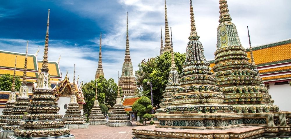 Colorful and ornate stupas of Wat Pho in Bangkok, Thailand, stand under a vibrant blue sky. The scene conveys a sense of tranquility and cultural richness.
