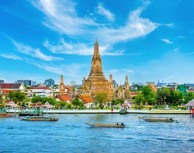A majestic temple with ornate spires stands by a serene river under a vibrant blue sky, boats gently floating, exuding a peaceful and historic aura.