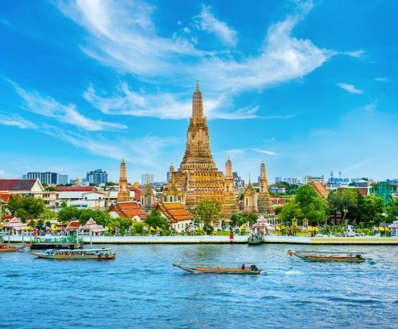 A majestic temple with ornate spires stands by a serene river under a vibrant blue sky, boats gently floating, exuding a peaceful and historic aura.