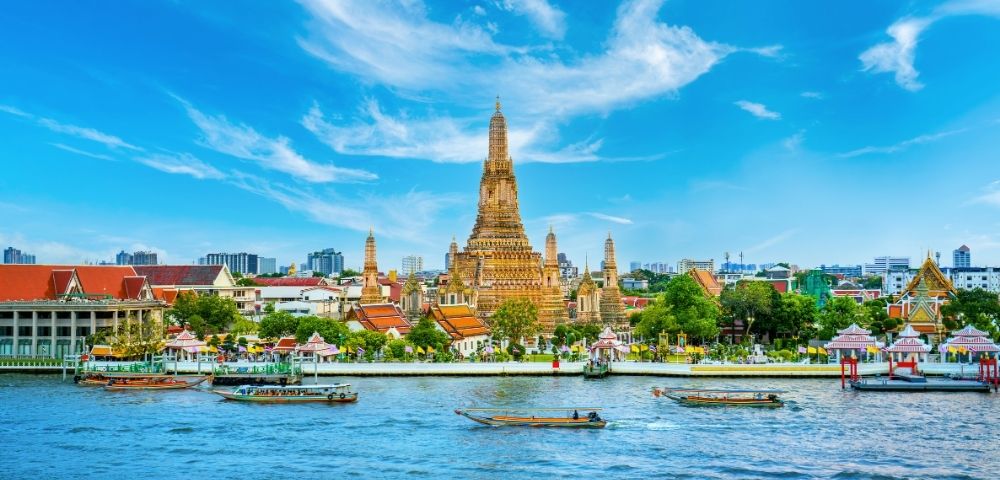 A majestic temple with ornate spires stands by a serene river under a vibrant blue sky, boats gently floating, exuding a peaceful and historic aura.
