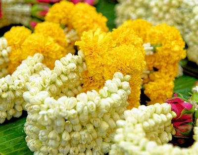 Flower garlands made of yellow marigolds and white jasmine buds are arranged side by side on green leaves, creating a vibrant and festive display.