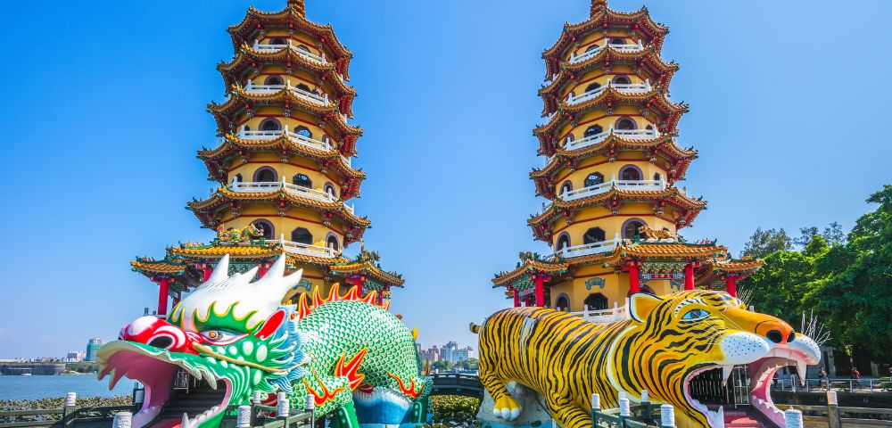 Two ornate pagodas stand side by side, each with vibrant dragon and tiger sculptures at their base, under a clear blue sky, creating a majestic and lively scene.
