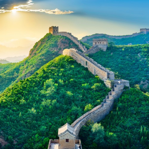 The Great Wall of China stretches across lush green hills under a vibrant, glowing sunset sky, evoking a sense of grandeur and timeless beauty.