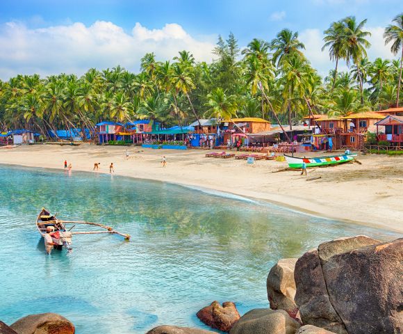 A serene beach with colorful huts, palm trees, and a vibrant shoreline. A small boat with fishermen is in the calm, clear water, conveying a peaceful ambiance.