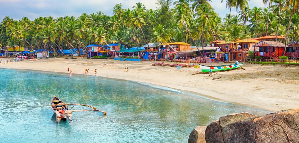 A serene beach with colorful huts, palm trees, and a vibrant shoreline. A small boat with fishermen is in the calm, clear water, conveying a peaceful ambiance.