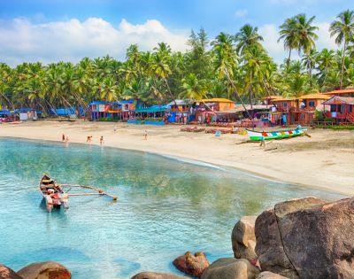 A serene beach with colorful huts, palm trees, and a vibrant shoreline. A small boat with fishermen is in the calm, clear water, conveying a peaceful ambiance.