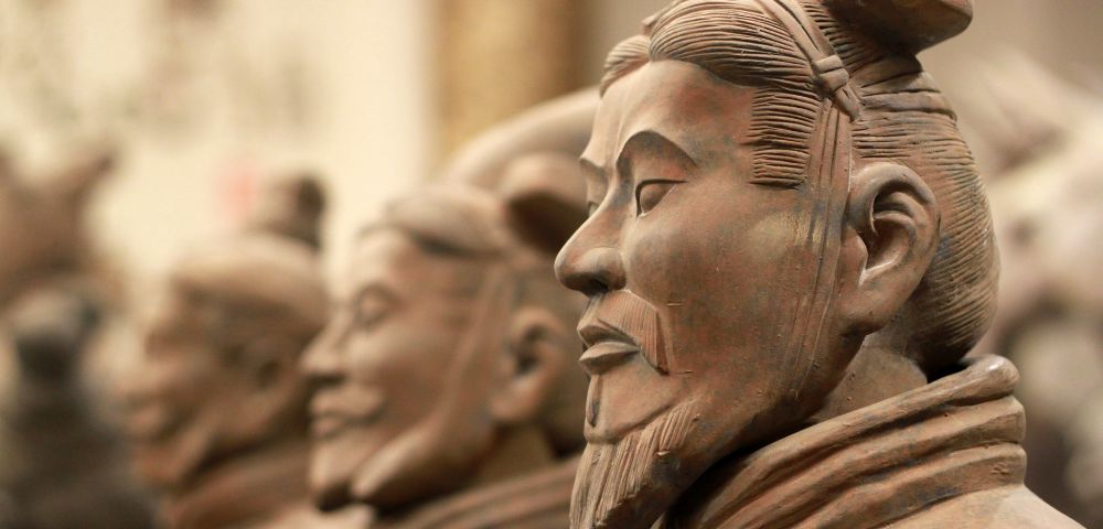 Close-up of Terracotta Warrior statues showing detailed facial features and traditional hairstyles. The statues convey a calm, stoic presence.