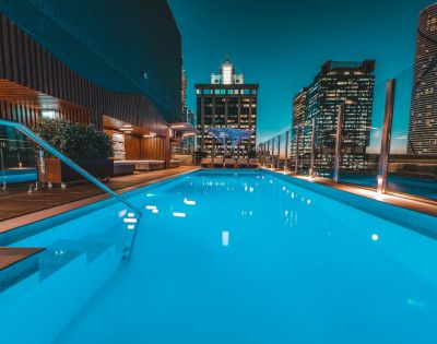Sparkling rooftop pool at night, surrounded by modern skyscrapers. The water glows turquoise under a serene city skyline with ambient lighting.